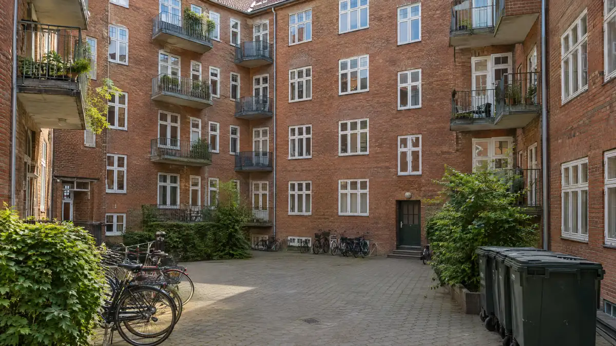Rød murstensejendom fra 1930'erne med altaner set fra gården med cykler